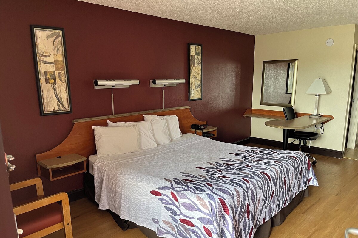 A hotel room with a large bed, wooden headboard, bedside tables, a desk, and a chair.