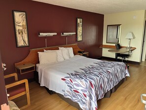 A hotel room with a large bed, wooden headboard, bedside tables, a desk, and a chair. - Red Roof Inn Virginia Beach - Norfolk Airport (Virginia Beach)