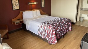 Una habitación de hotel con una cama de madera, una mesita de noche, una lámpara de pared y una obra de arte enmarcada sobre la cama.