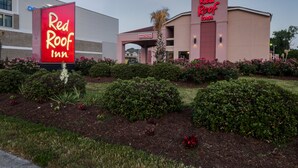 Un hotel Red Roof Inn con un cartel de recepción, un estacionamiento y jardines ajardinados.