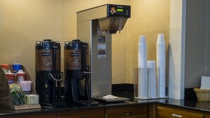 Una estación de café con dos máquinas de café Bunn, un dispensador de café y una pila de vasos desechables.