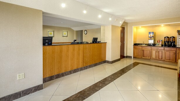 Un hall de hotel con mostrador de recepción, un reloj y una zona de cocina con electrodomésticos.