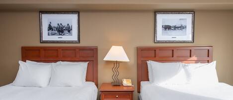 Una habitación de hotel con dos camas, una mesita de noche con lámpara y dos cuadros en la pared.