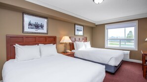 A hotel room with two beds, a nightstand with a lamp, a framed picture on the wall, and a large window. - Coast Edson Hotel (Edson)