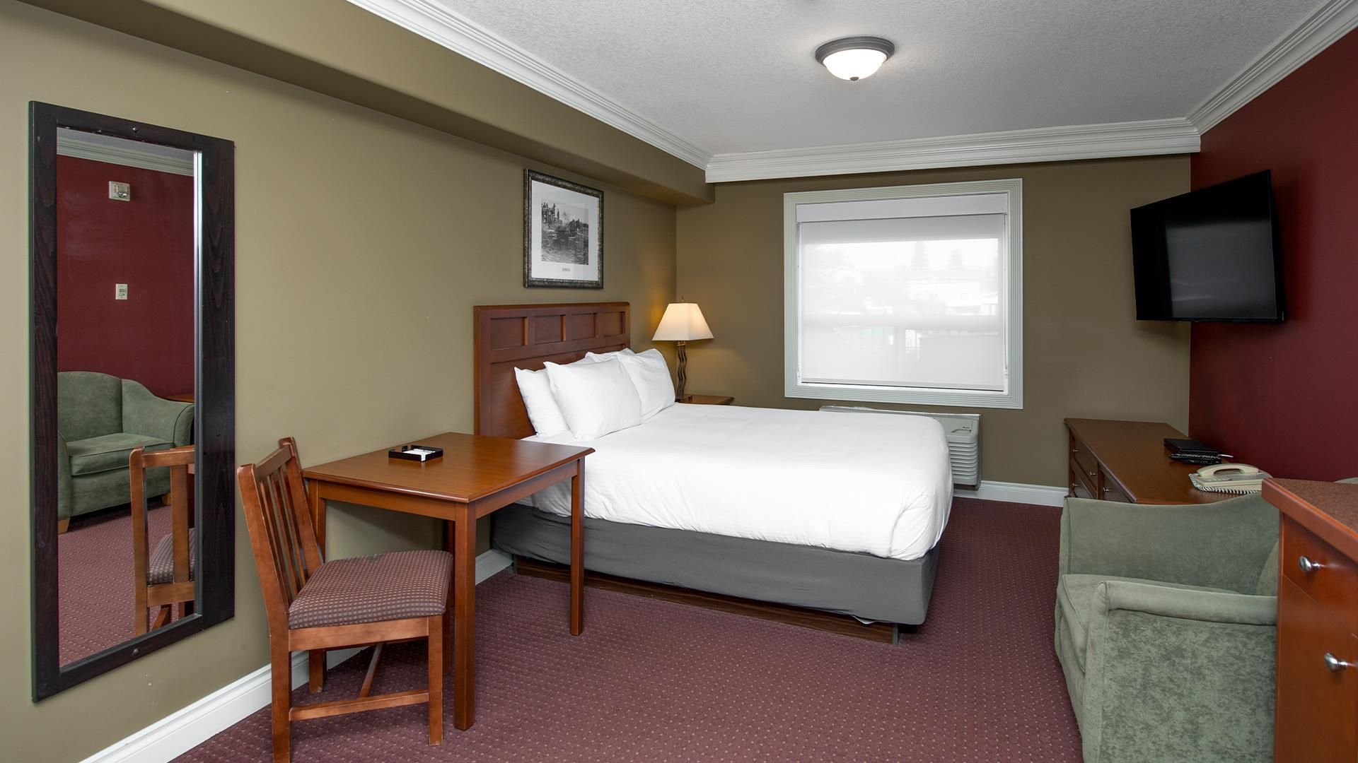 Ein Hotelzimmer mit Bett, Schreibtisch, Stuhl, Fernseher und einem Fenster.