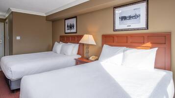 A hotel room with two beds, a nightstand with a lamp, and framed pictures on the wall.