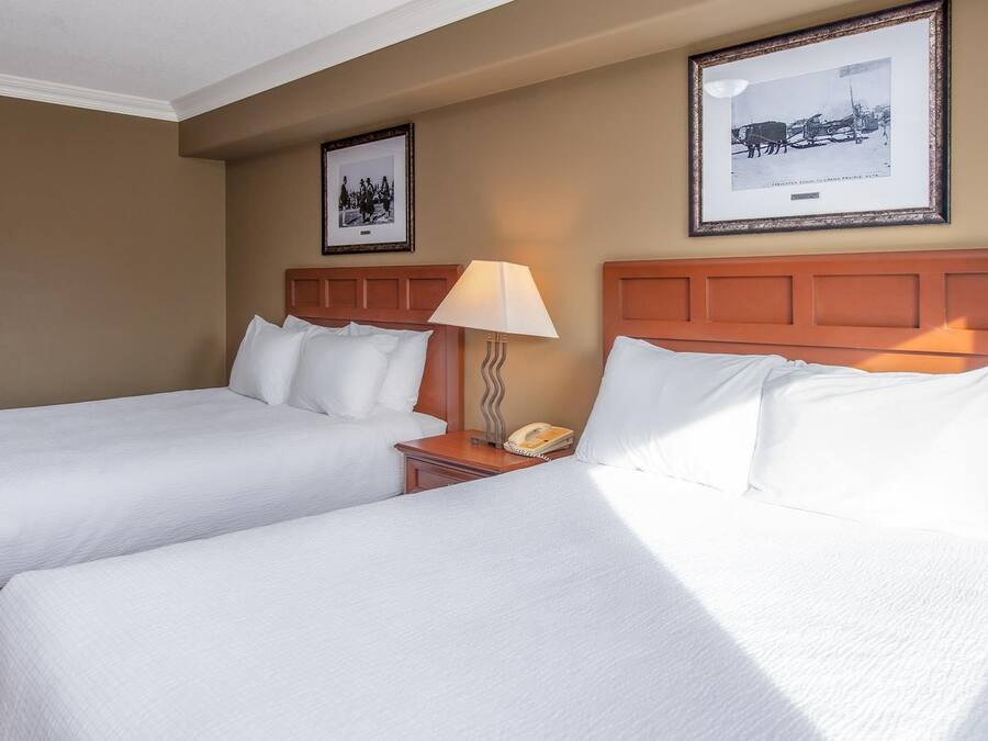 A hotel room with two beds, a nightstand with a lamp, and framed pictures on the wall.