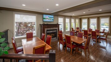 Un espace repas avec des tables en bois et des chaises rouges, une cheminée et de grandes fenêtres.