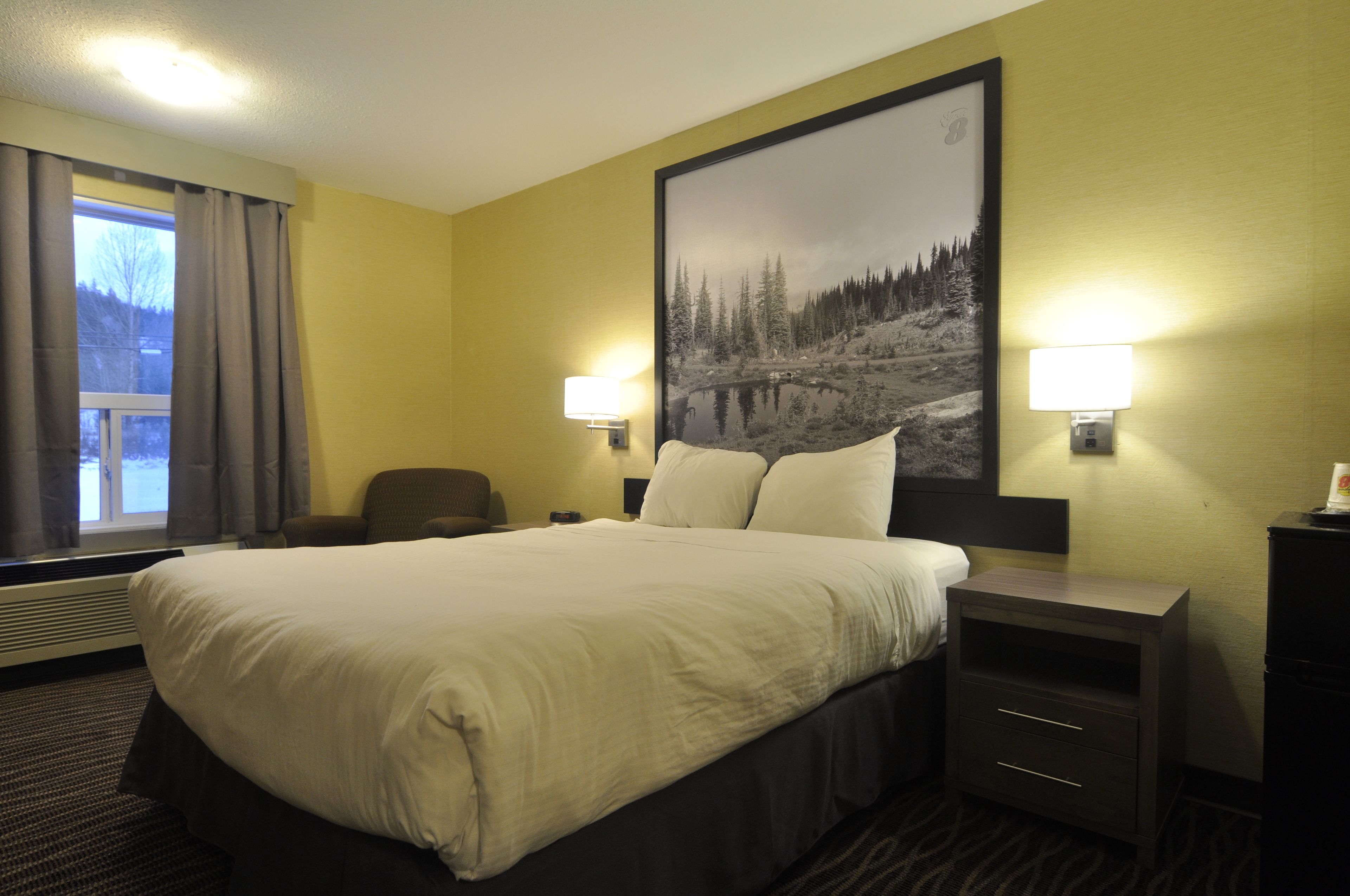 A hotel room with a large bed, two bedside lamps, a chair, a nightstand, and a large framed picture on the wall.