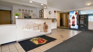 Zona de recepción de un hotel con un mostrador blanco, un refrigerador de Coca-Cola y el logotipo de Super 8 en el felpudo.