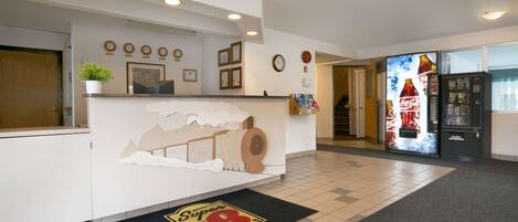 A hotel reception area with a white counter, a Coca-Cola refrigerator, and a Super 8 logo on the floor mat.
