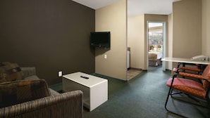 Habitación de hotel con televisor, una mesita, un sofá a rayas y un sillón estampado.