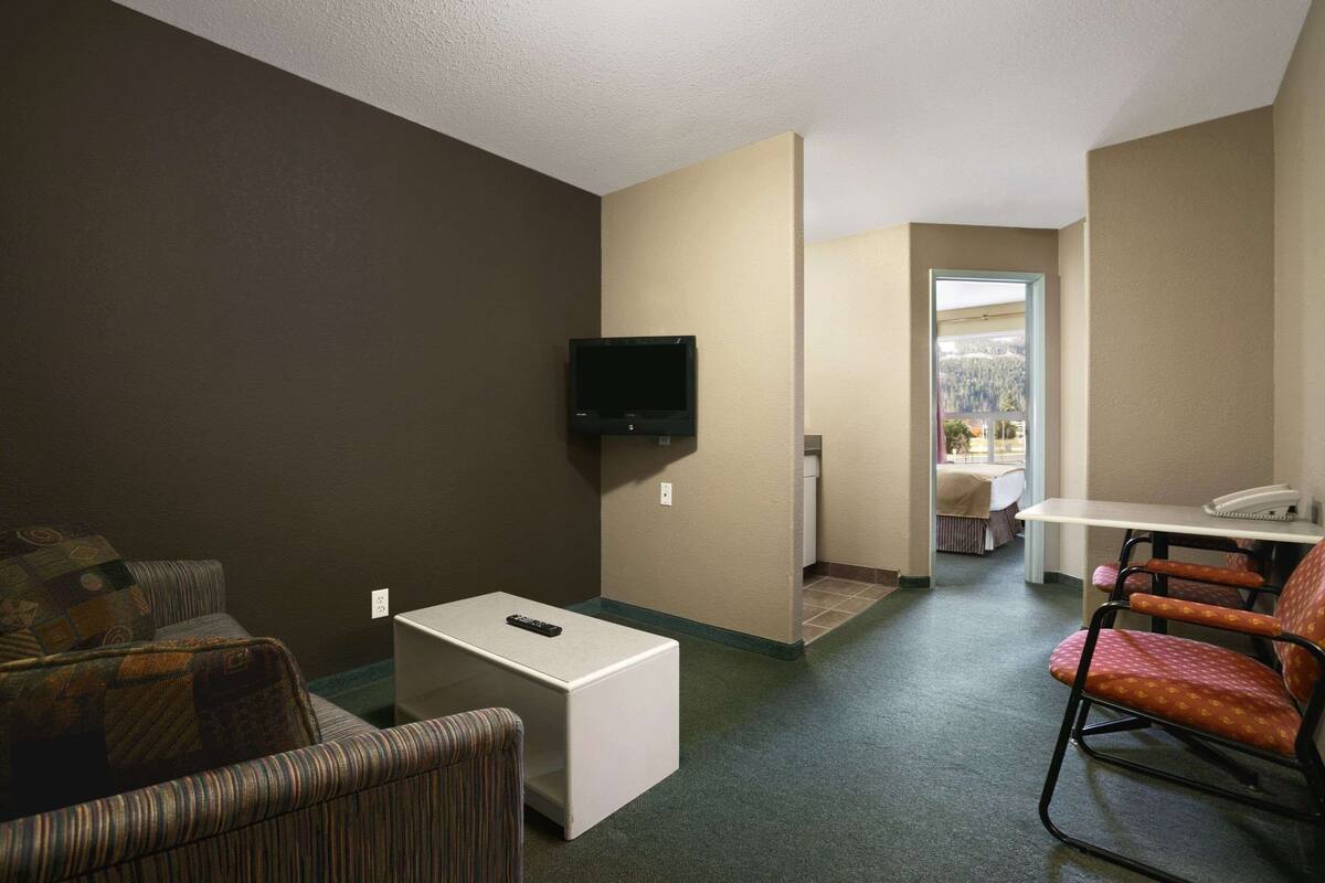 Quarto de hotel com televisão, uma pequena mesa, um sofá listrado e uma poltrona estampada.