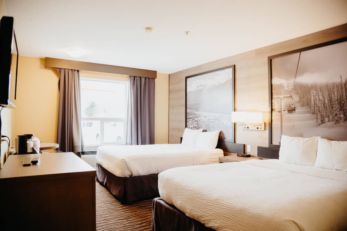 Quarto de hotel com duas camas, uma mesa, uma cadeira, uma televisão e uma janela com cortinas.