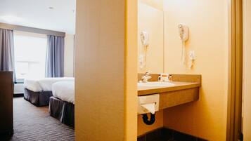 A hotel room with a bed, a bathroom with a sink and a hairdryer, and a window with curtains.