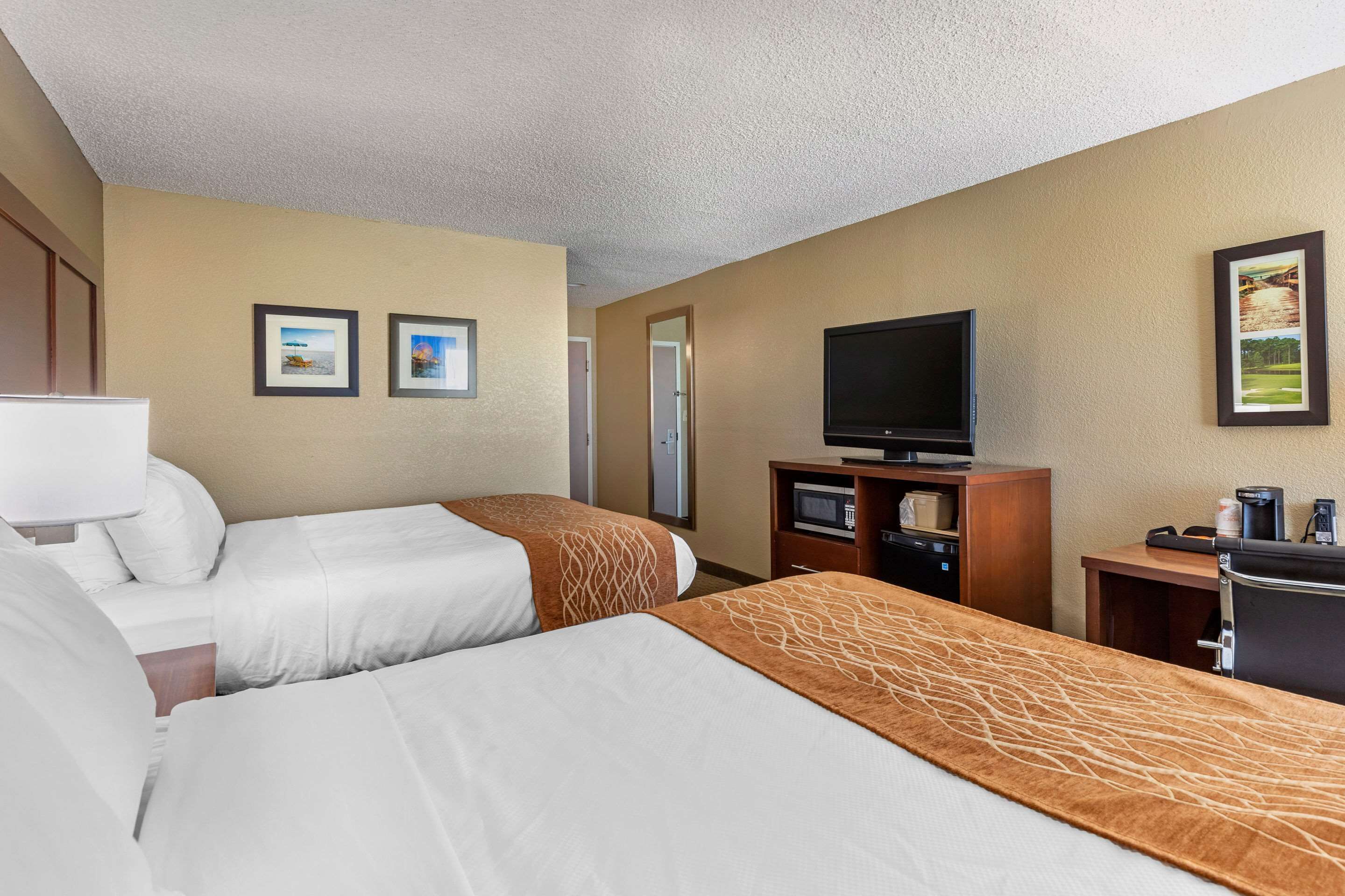 A hotel room with two beds, a television, a desk, and a microwave.