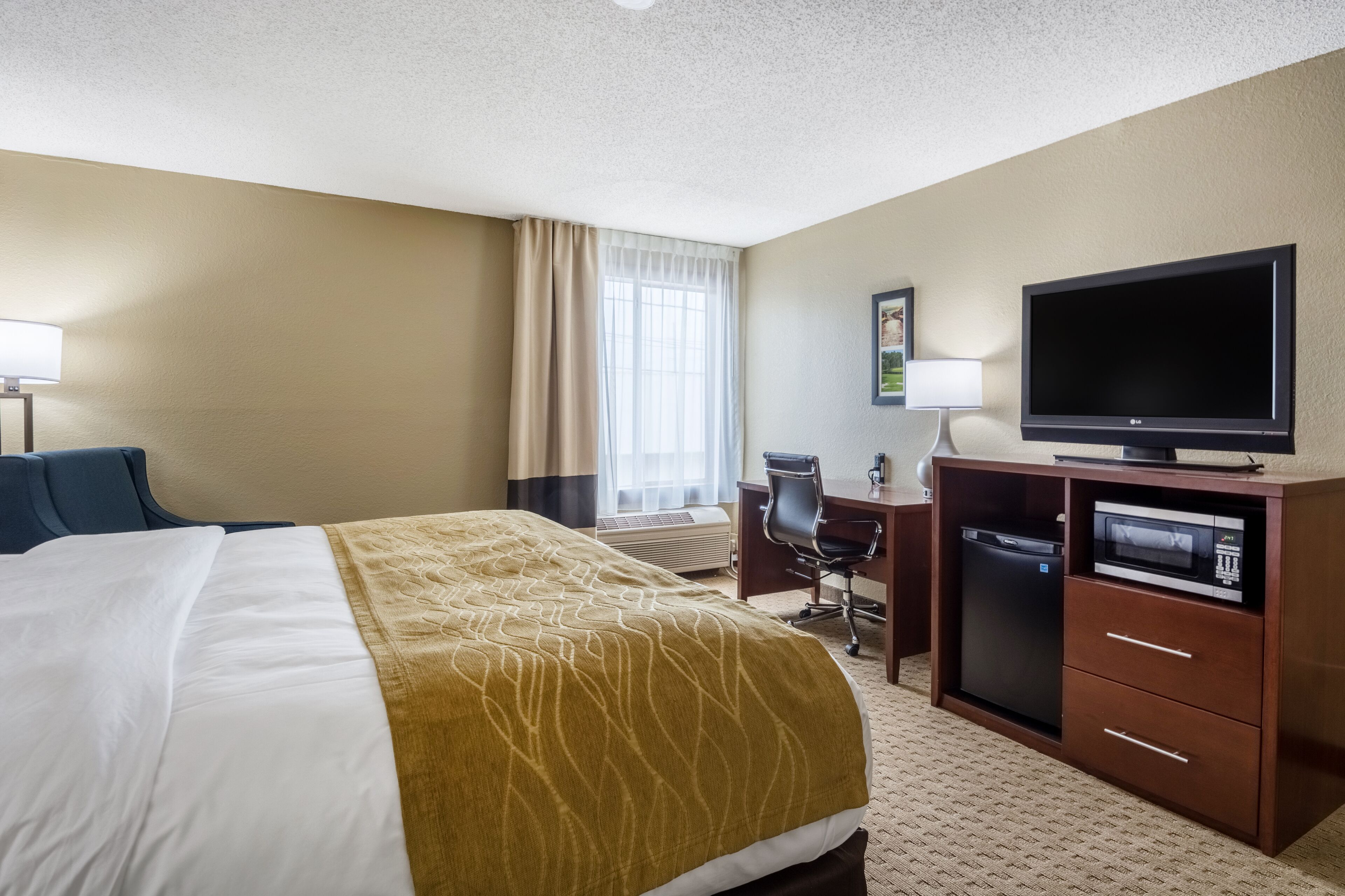 Quarto de hotel com uma cama, uma escrivaninha com computador, televisão e micro-ondas.