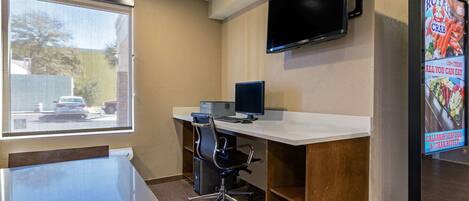 A hotel room with a desk, chair, and a flat-screen TV mounted on the wall.