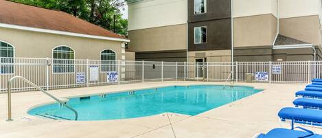 A swimming pool with blue water, surrounded by a white fence, and blue lounge chairs.