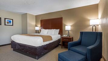 A hotel room with a large bed, a nightstand with a lamp, and a blue armchair.