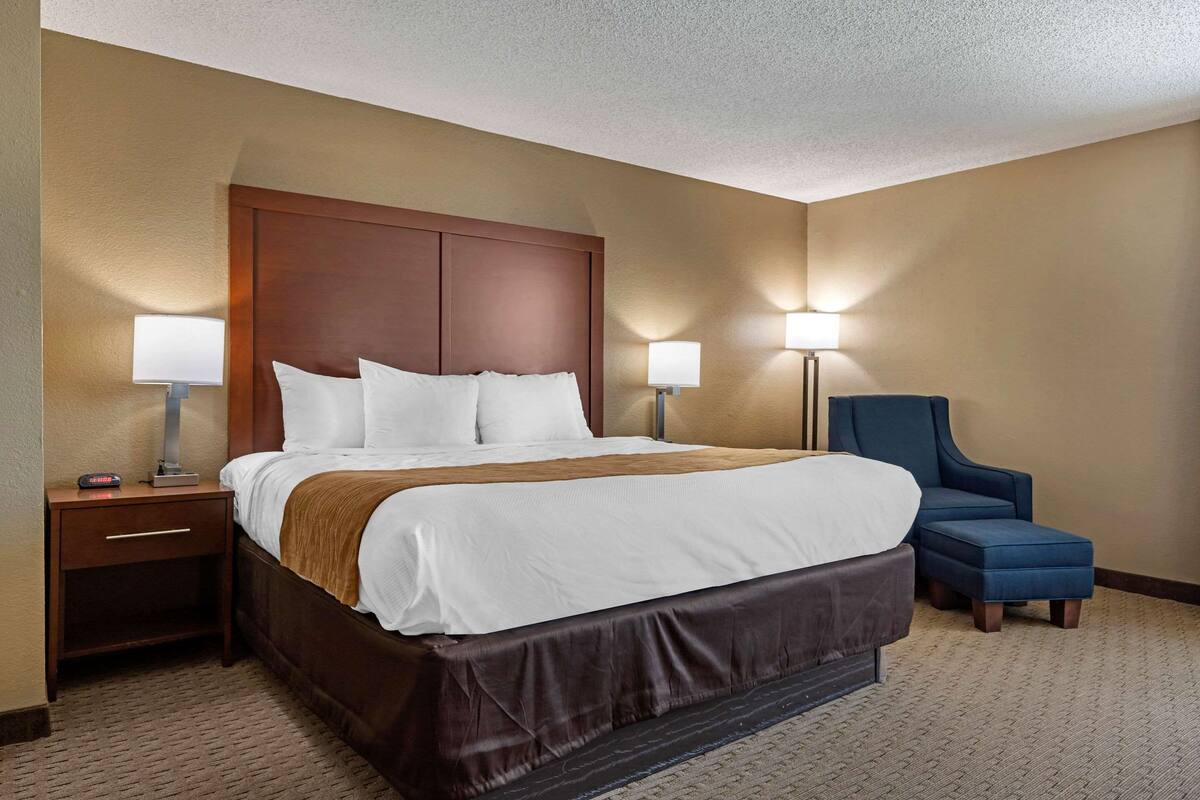 Une chambre d’hôtel avec un grand lit, deux tables de chevet, un bureau, une chaise et deux lampes fixées au mur.