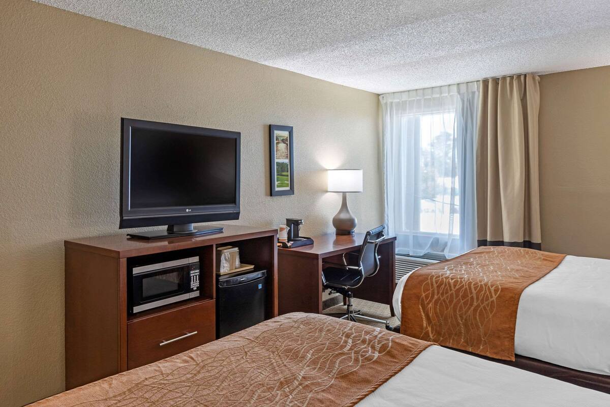 Une chambre d’hôtel avec deux lits, une télévision, un bureau avec une lampe, un four à micro-ondes et un petit réfrigérateur.