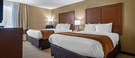 A hotel room with two beds, a desk, and a TV.