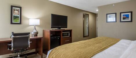 Habitación de hotel con cama, escritorio, silla, televisor y espejo.
