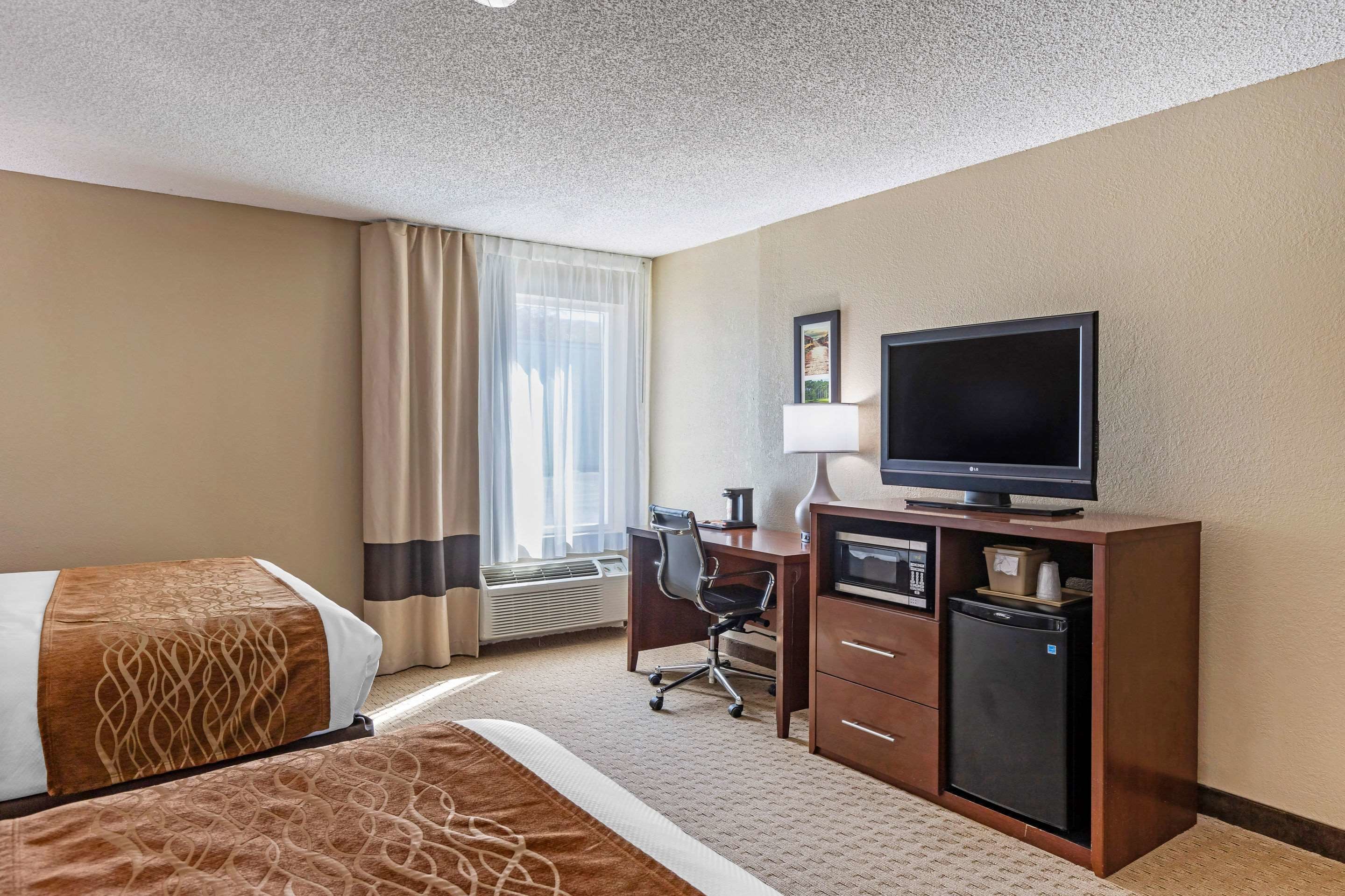 A hotel room with a bed, a desk with a computer, a TV, and a mini-fridge.