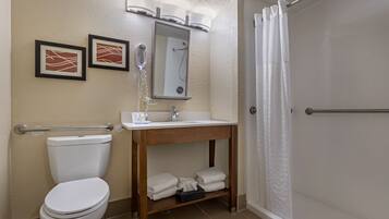 A bathroom with a toilet, sink, and shower. There are framed pictures on the wall, a towel rack, and a mirror above the sink.