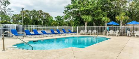 A swimming pool with blue and white lounge chairs, surrounded by a white fence and trees.