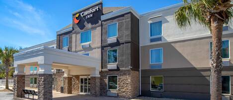 A Comfort Inn hotel with a modern design, featuring a covered entrance and a palm tree in front.