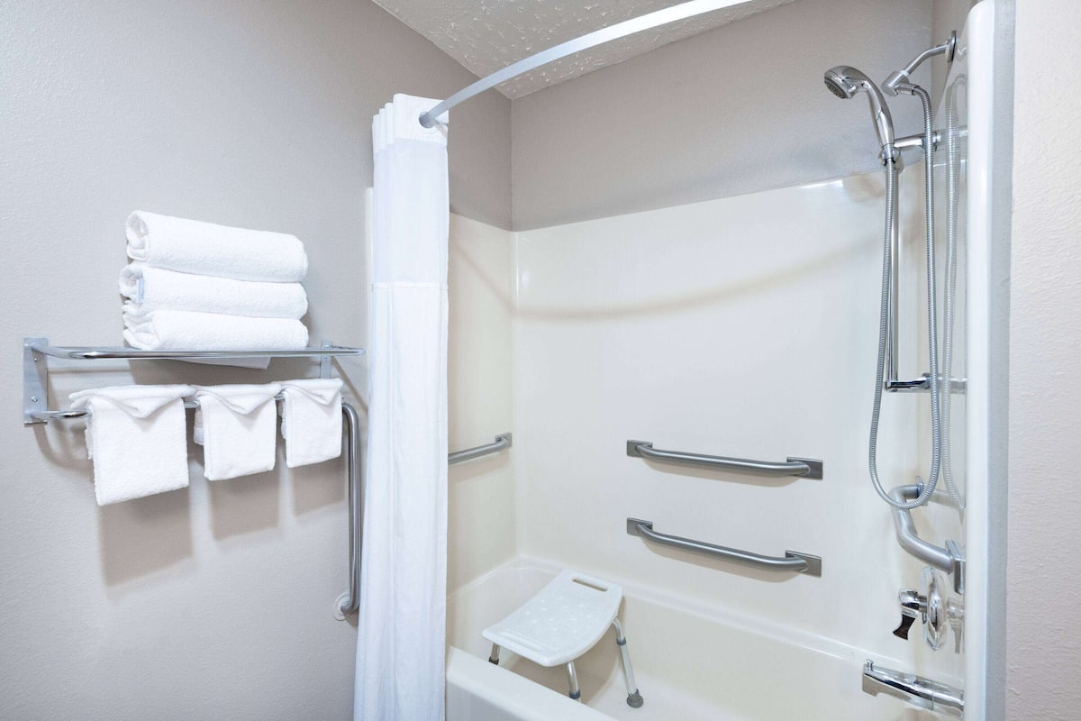 A modern bathroom with a glass-enclosed shower, a white bathtub, and a shelf with neatly folded towels.