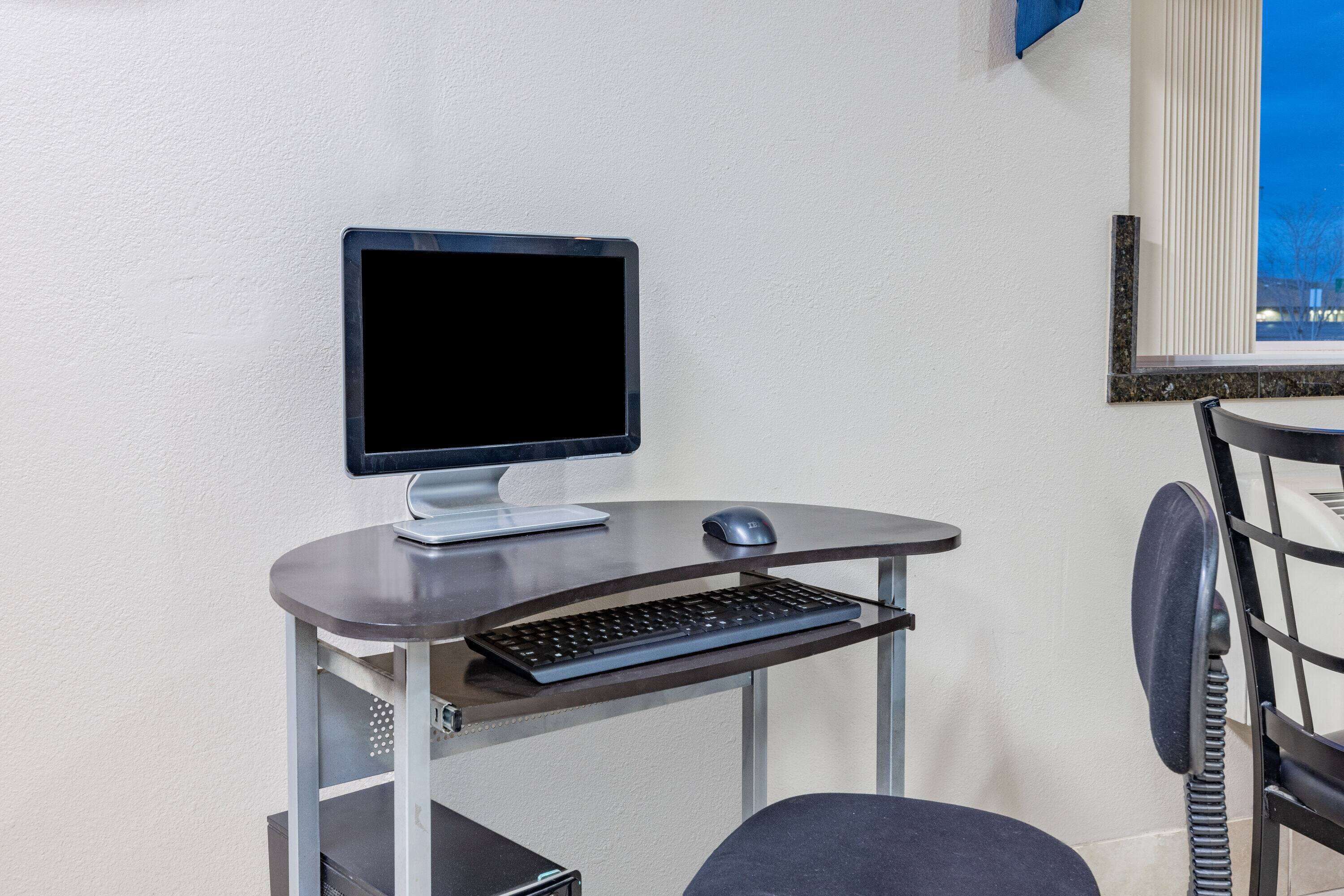 Ein kleiner, moderner Arbeitsplatz mit Computer, Tastatur und Maus auf einem Metalldruck, vor einer weißen Wand.