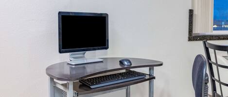Un pequeño espacio de trabajo moderno con una computadora, teclado y ratón sobre un escritorio metálico frente a una pared blanca.