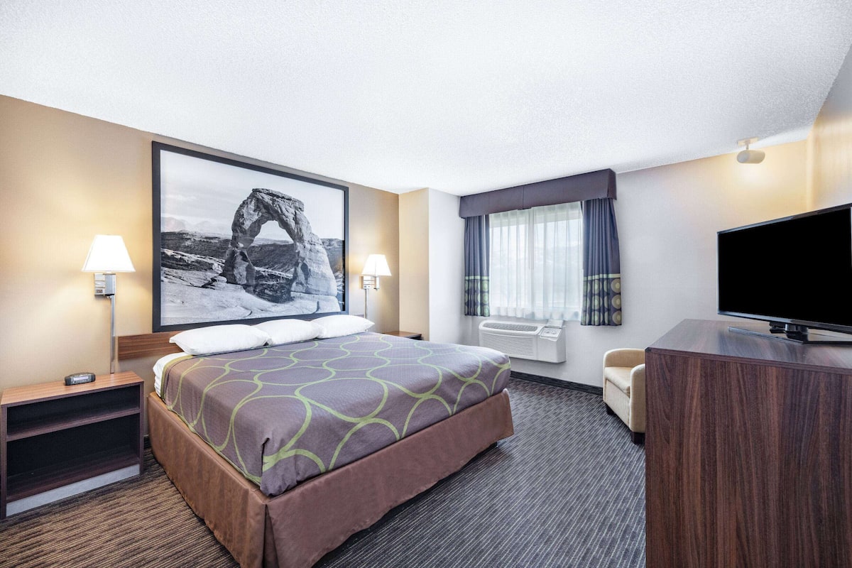 A hotel room with a large bed, two bedside lamps, a flat-screen TV, a desk, and a window with curtains.
