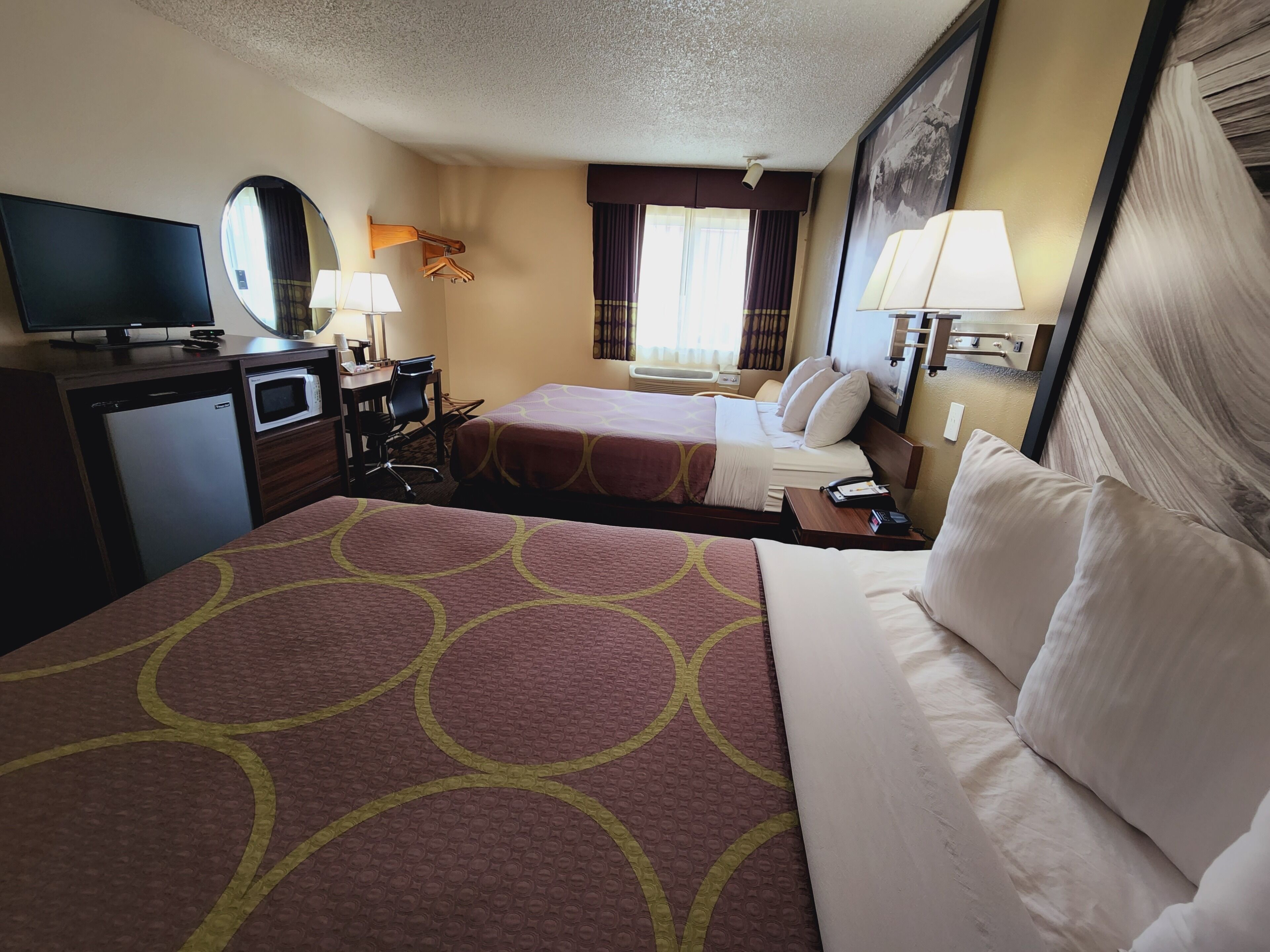 A hotel room with two beds, a desk, a television, a microwave, and a window with curtains.