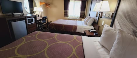 A hotel room with two beds, a desk, a television, a microwave, and a window with curtains.