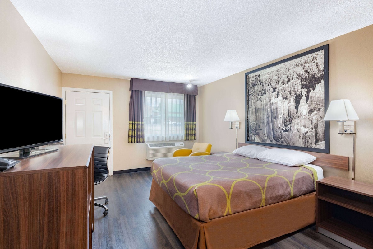 A hotel room with a bed, a desk, a television, and a large window with curtains.