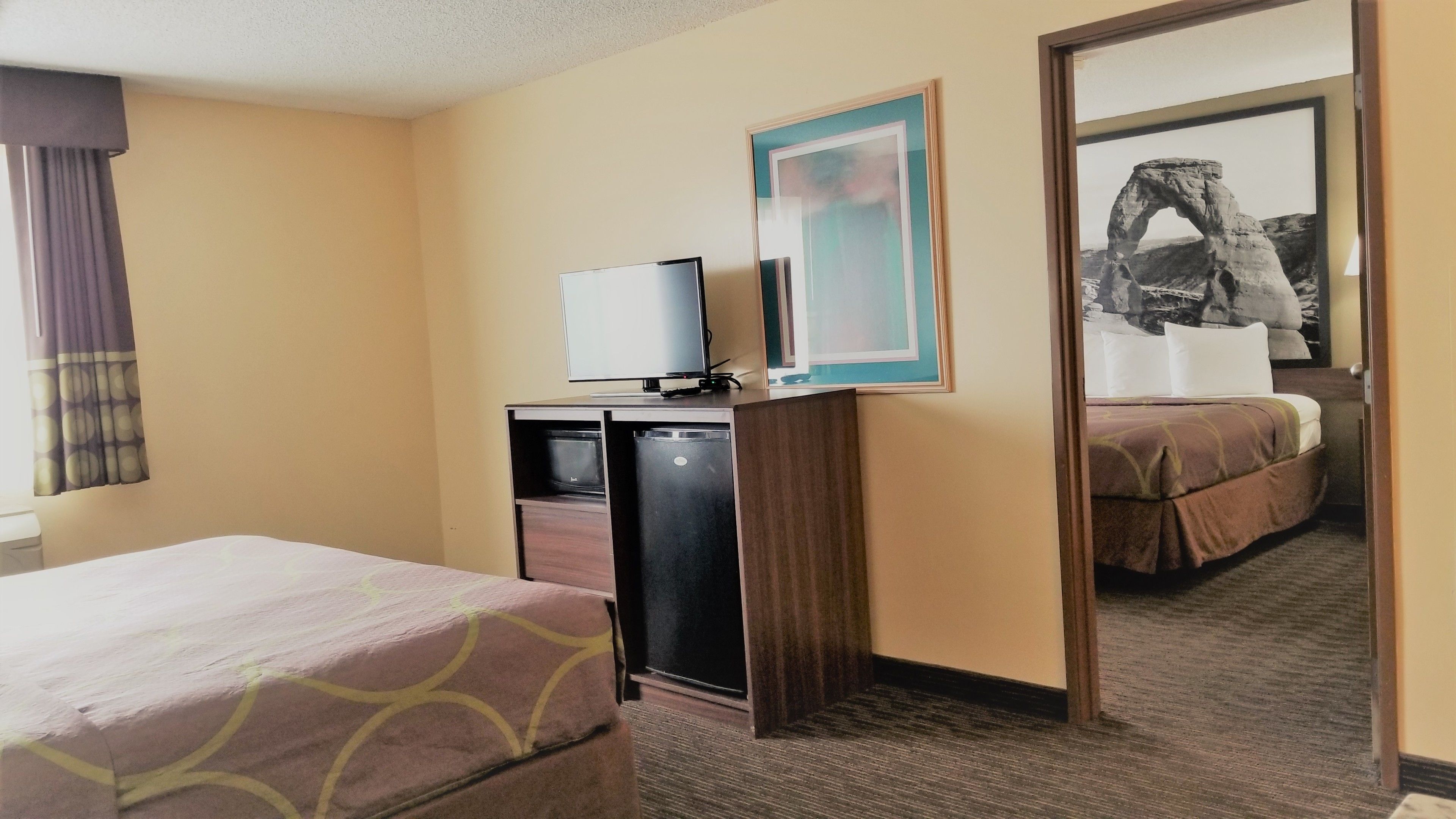 A hotel room with two beds, a television, a small desk with a computer, and a framed picture on the wall.