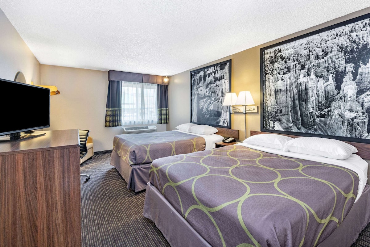 A hotel room with two beds, a desk, a television, and artwork on the walls.