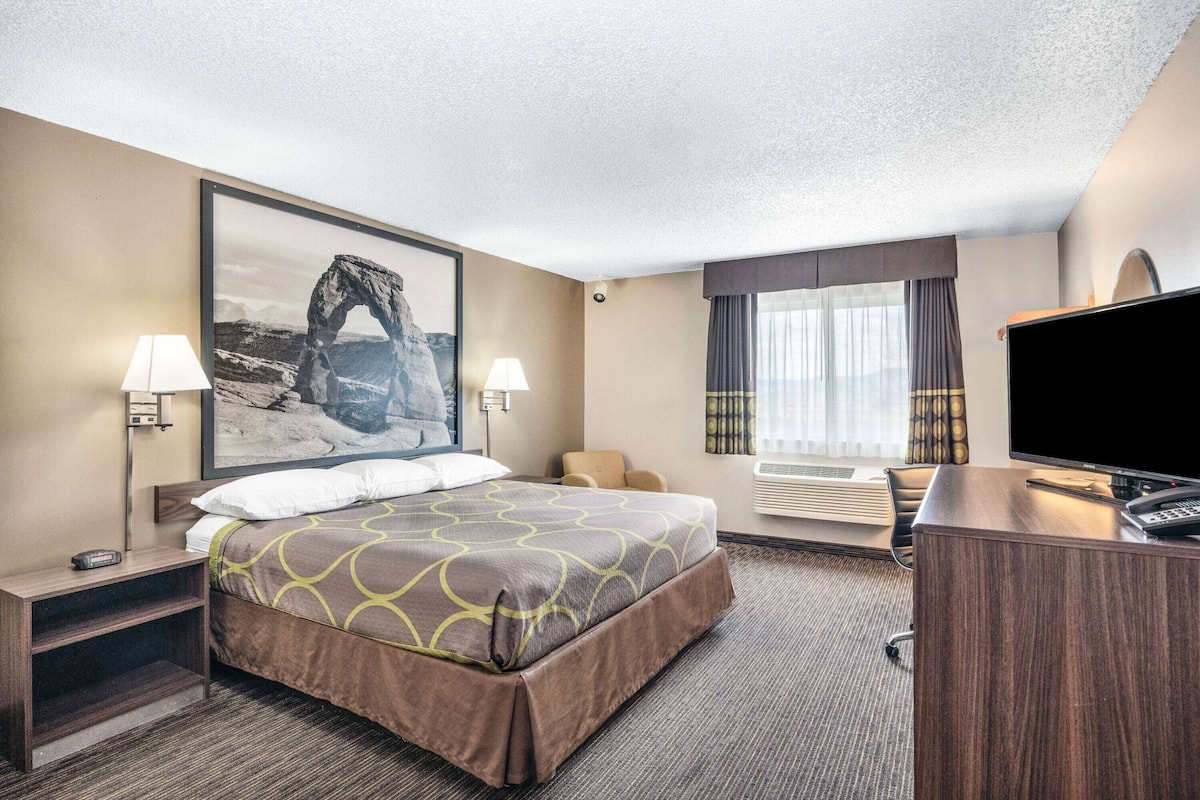 A hotel room with a bed, a desk, a television, and a large framed picture on the wall.