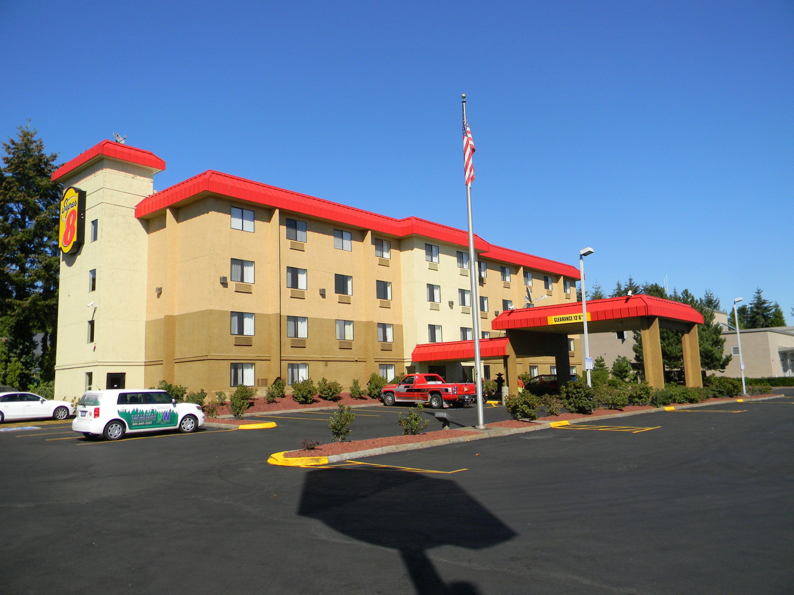 A hotel with a red roof and beige walls, a parking lot with marked spaces, and a clear blue sky.