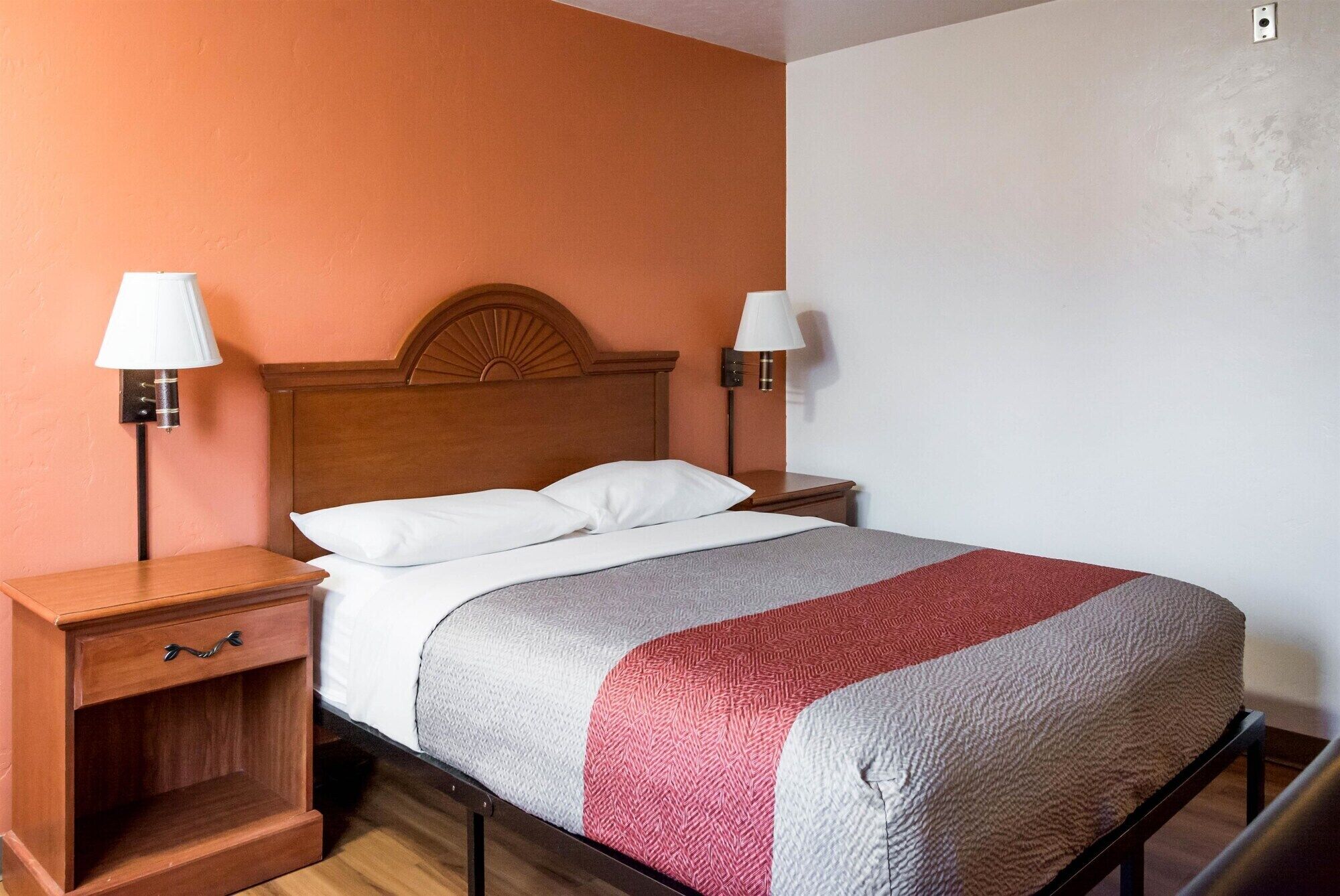 Un lit bien fait, avec une tête de lit en bois, deux tables de chevet avec des lampes et une petite table de nuit dotée d’un tiroir.