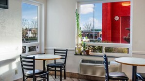 A corner of a cafe with two tables and chairs, a red curtain, and a view of the street outside. - Motel 6 Wilsonville, OR - Portland (Wilsonville)