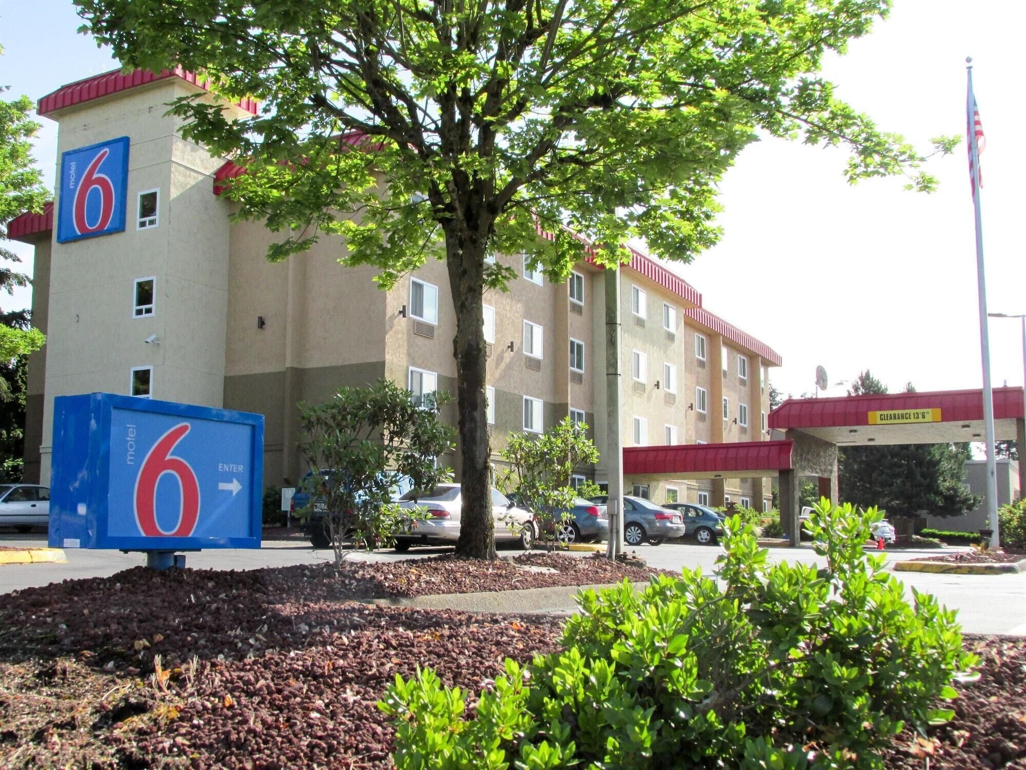 A motel with a large '6' sign, a parking area, and a building with multiple windows and a red roof.
