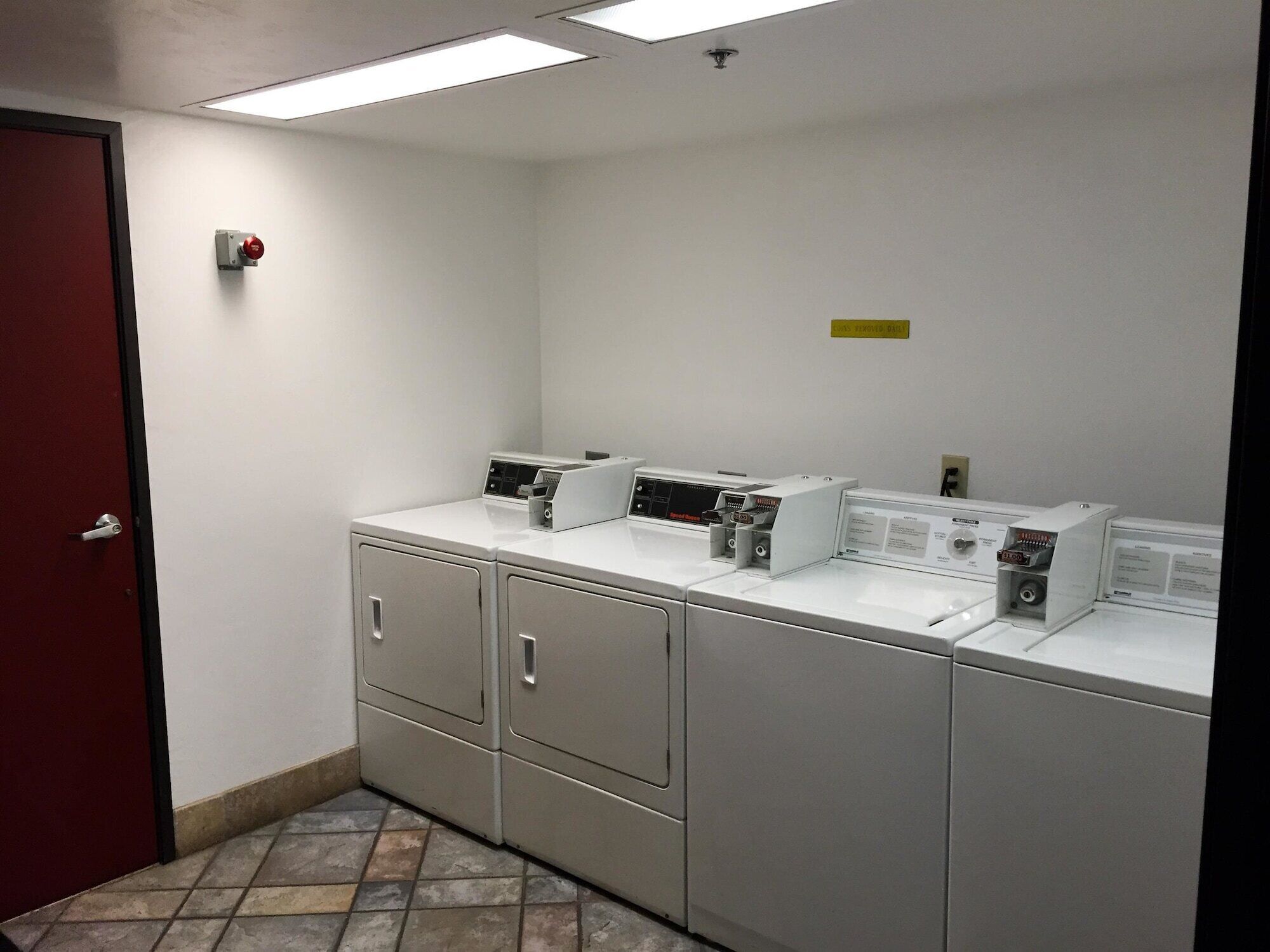 A laundry room with four washing machines, a red door, and a ceiling light.