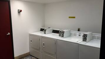 A laundry room with four washing machines, a red door, and a ceiling light.