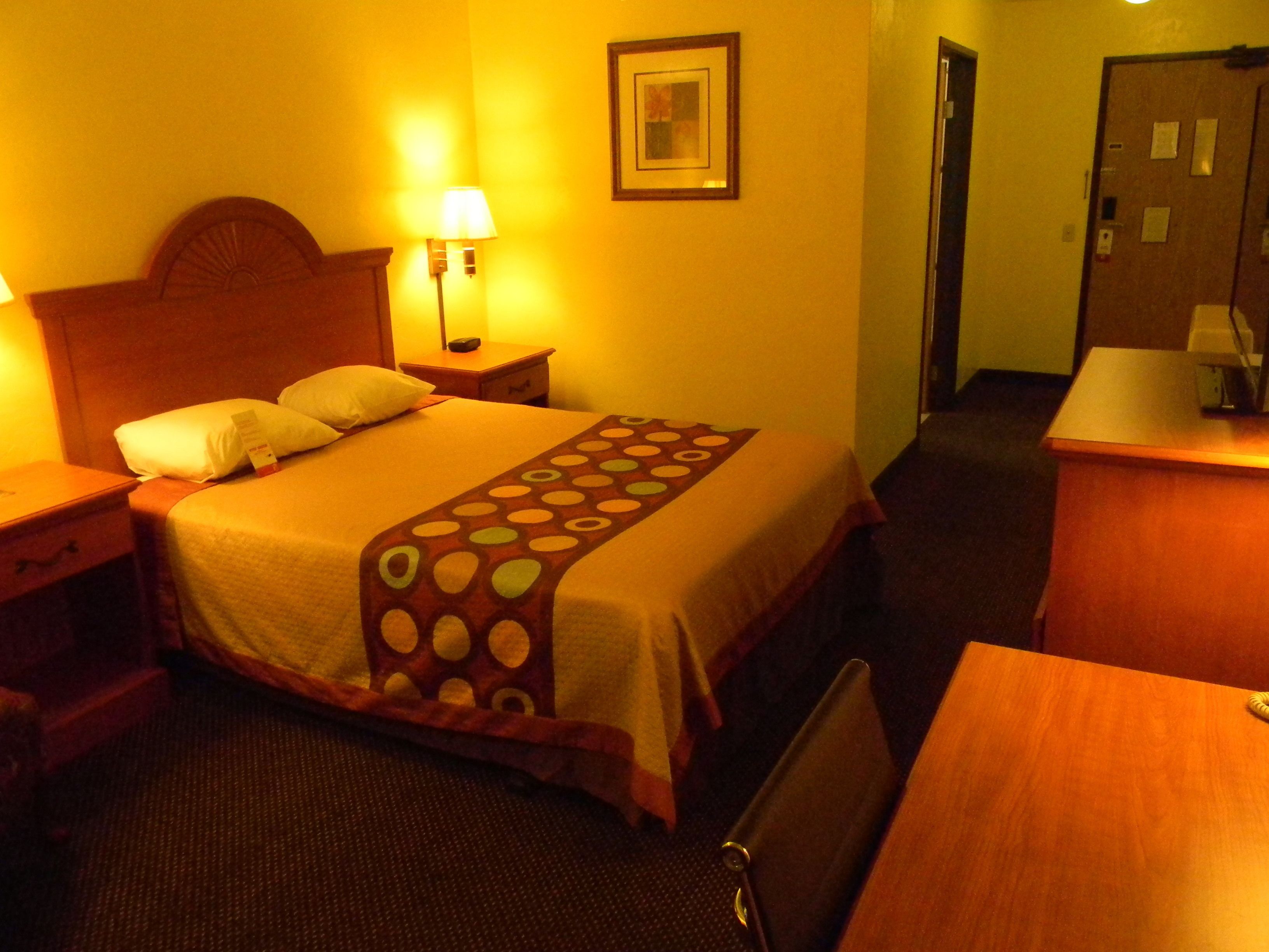 A hotel room with a bed, a nightstand, a desk, and a chair.