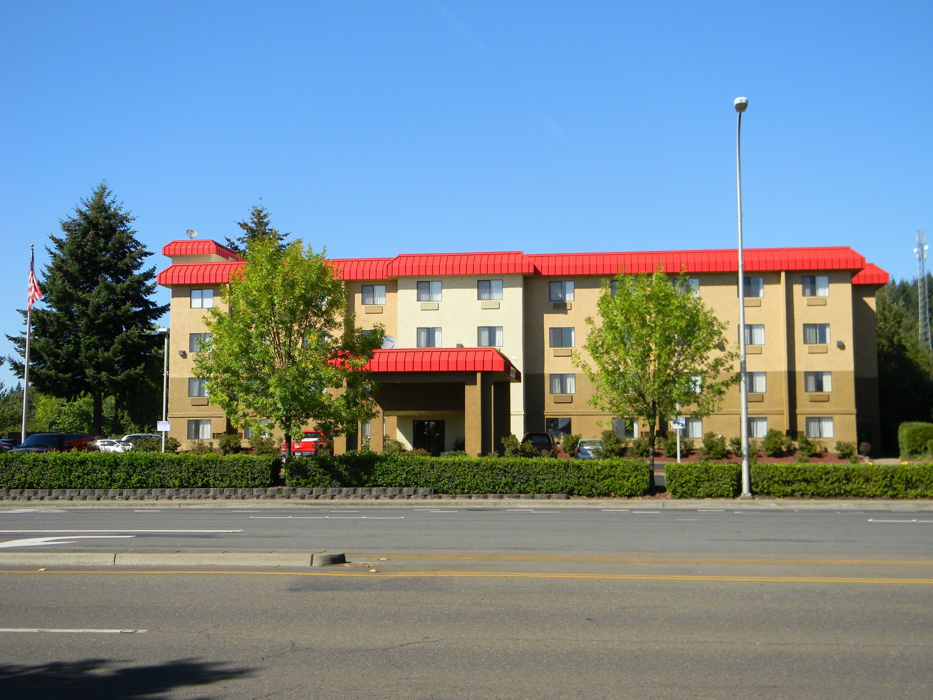 Un hotel de varios pisos con techo rojo y paredes color crema, que presenta una entrada central con toldo rojo.